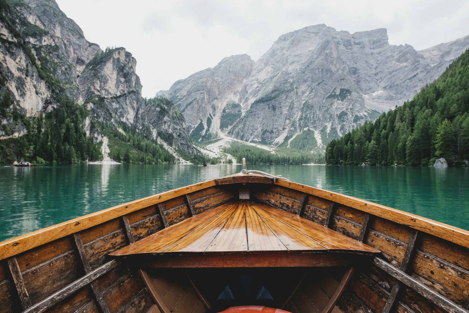 The bow of a wooden boat on a green alpine lake.