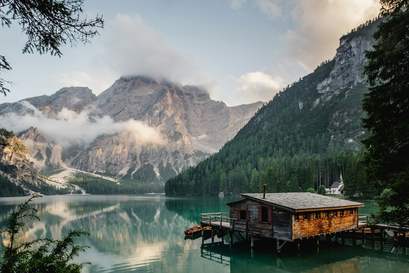 A still alpine lake at dusk with a wooden boathouse and cliffs reflected in the water.